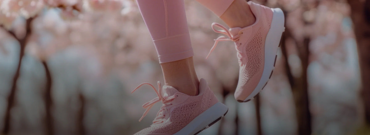 Pink sneakers worn with light pink pants against a blurred natural background